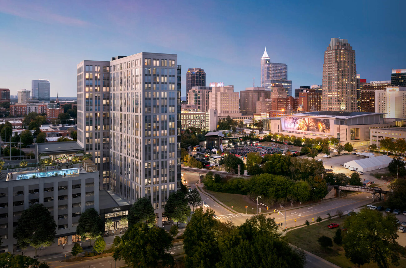 High up view of West Lenoir in the evening surrounded by the lit up city. The view of West Lenoir includes the parking garage and rooftop pool.